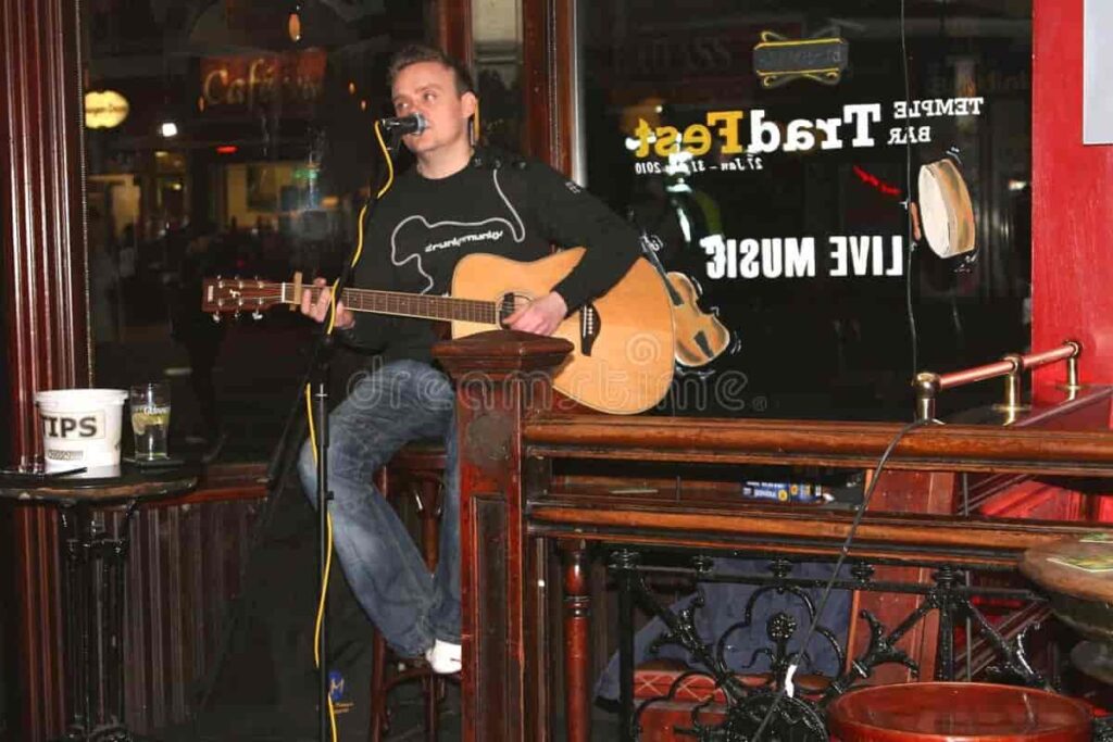 Musician performing live in a bar, playing an acoustic guitar and singing into a microphone.