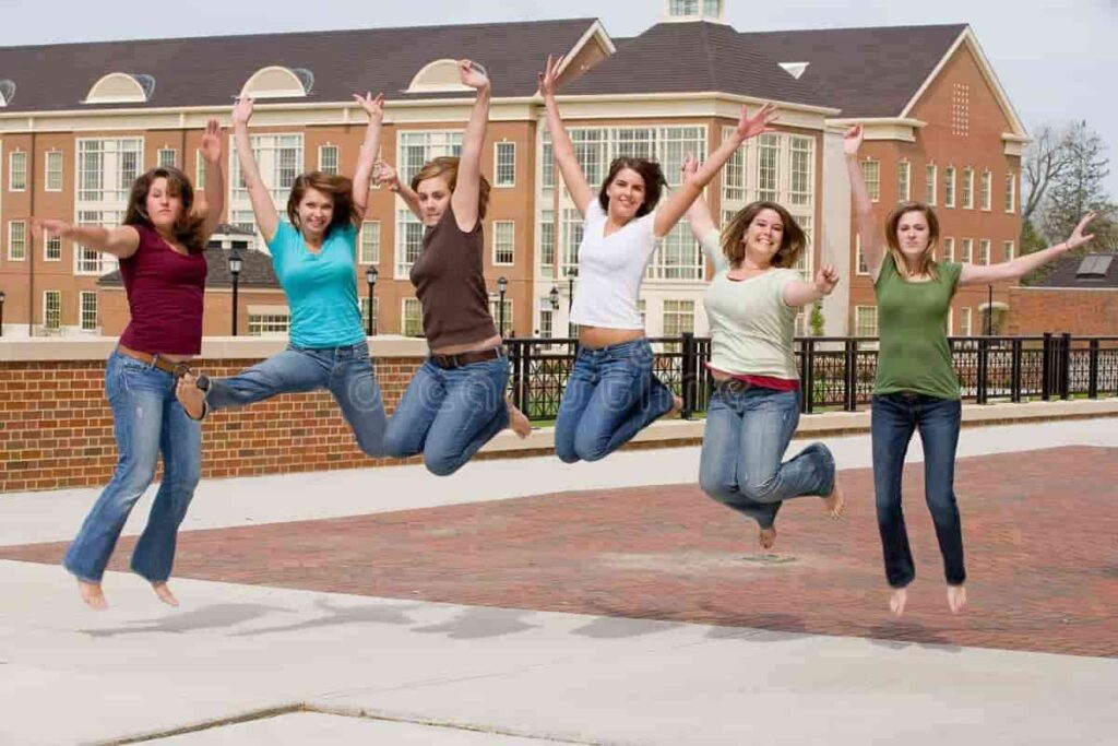 Group of happy female students jumping together on a university campus, celebrating friendship and student life.