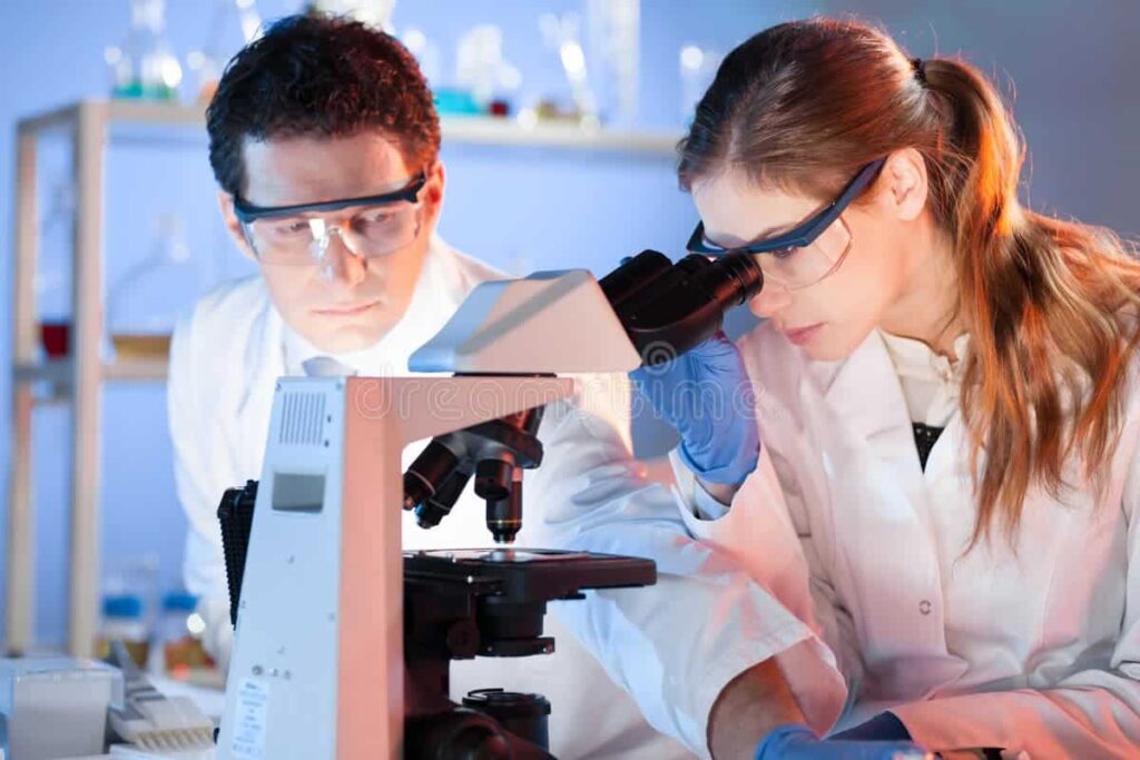 Two scientists in lab coats using a microscope in a modern research laboratory.