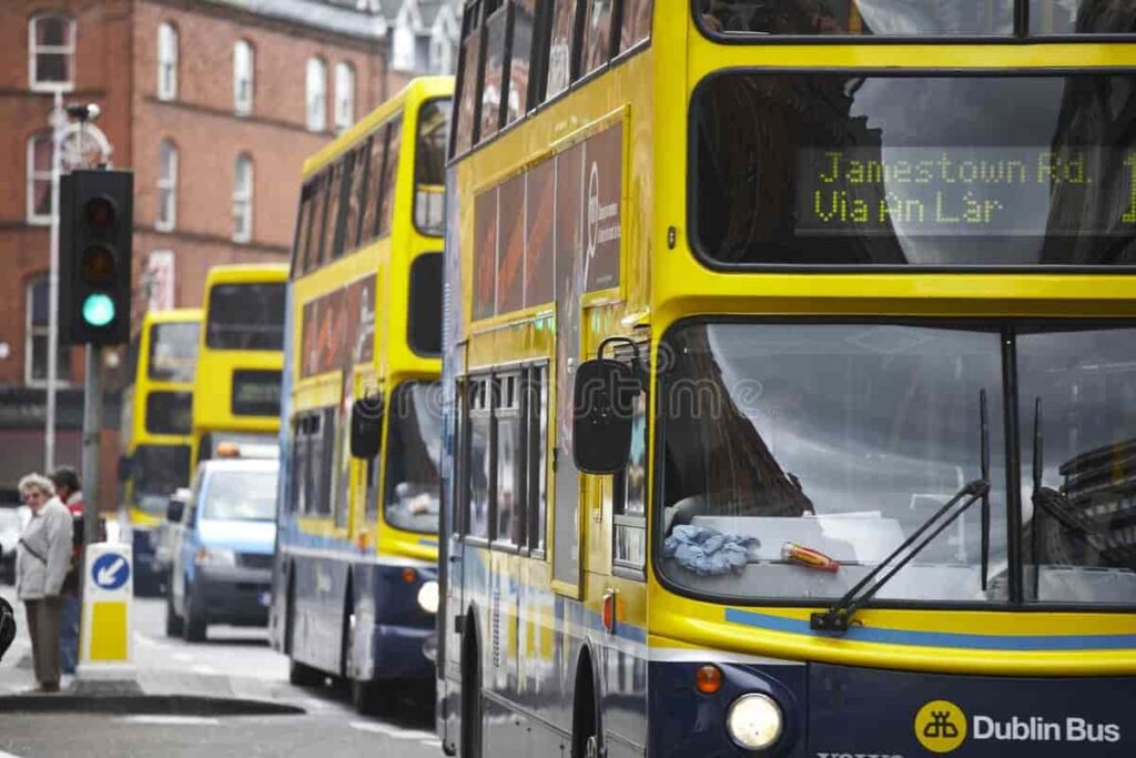 Yellow double-decker Dublin buses on a city street in Ireland, with a traffic light and pedestrians in the background.