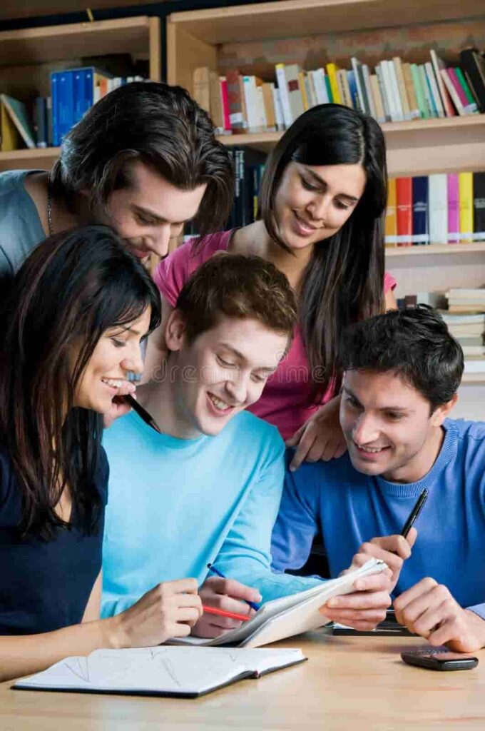 Group of international students studying together in a library, smiling and sharing notes.