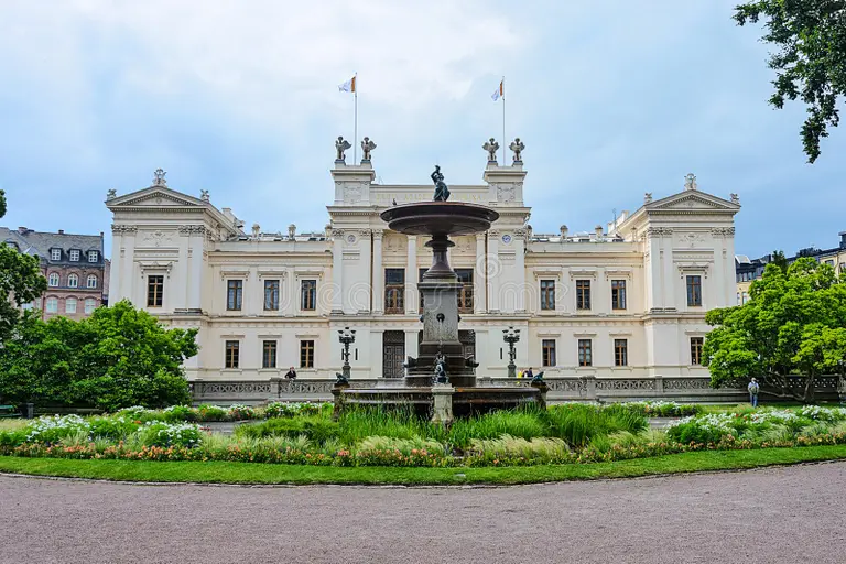 Lund University main building with central fountain in Lundagård Park, Lund, Sweden, on a cloudy day.