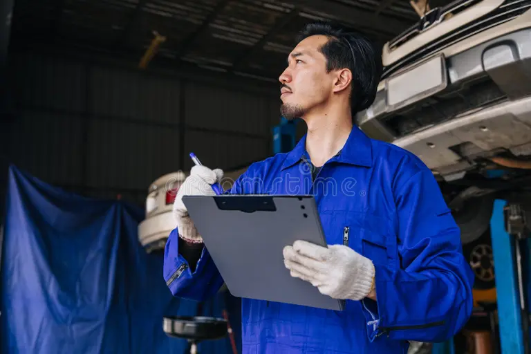 Technician in blue coveralls with a clipboard inside an auto workshop—post-study jobs & PR pathways for Study in Singapore.