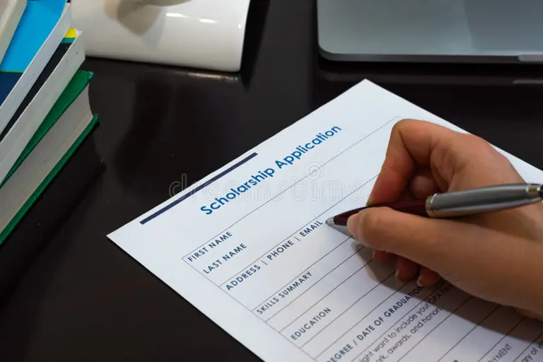 Hand filling a scholarship application form on a desk with books and a laptop—tuition, scholarships, and budgeting for Study in Sweden.