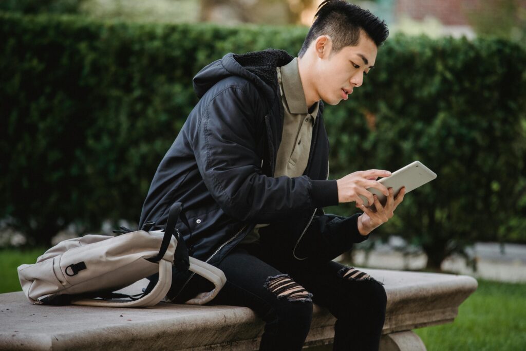 A student sitting outdoors using a tablet to download free UAE study PDF guides — representing education and digital learning.
