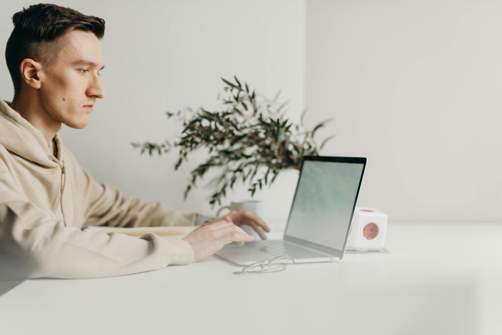 A focused student wearing a beige hoodie working on a laptop at a clean white desk, representing productivity and preparation for study abroad opportunities.