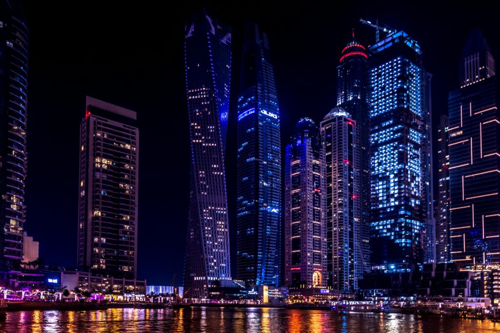 Vibrant Dubai skyline at night with illuminated high-rise buildings reflecting on the water, symbolizing global exposure and cultural diversity.