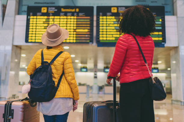 Two students at an airport looking at a flight departure board, symbolizing visa and documentation completion for studying in India.
