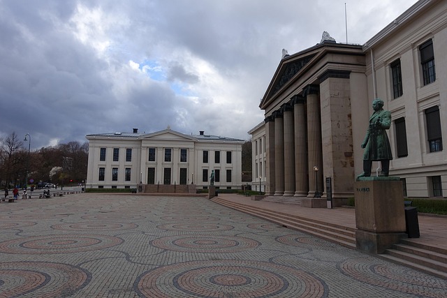 The University of Oslo main building with neoclassical architecture and a statue in front, under a cloudy sky in Norway.