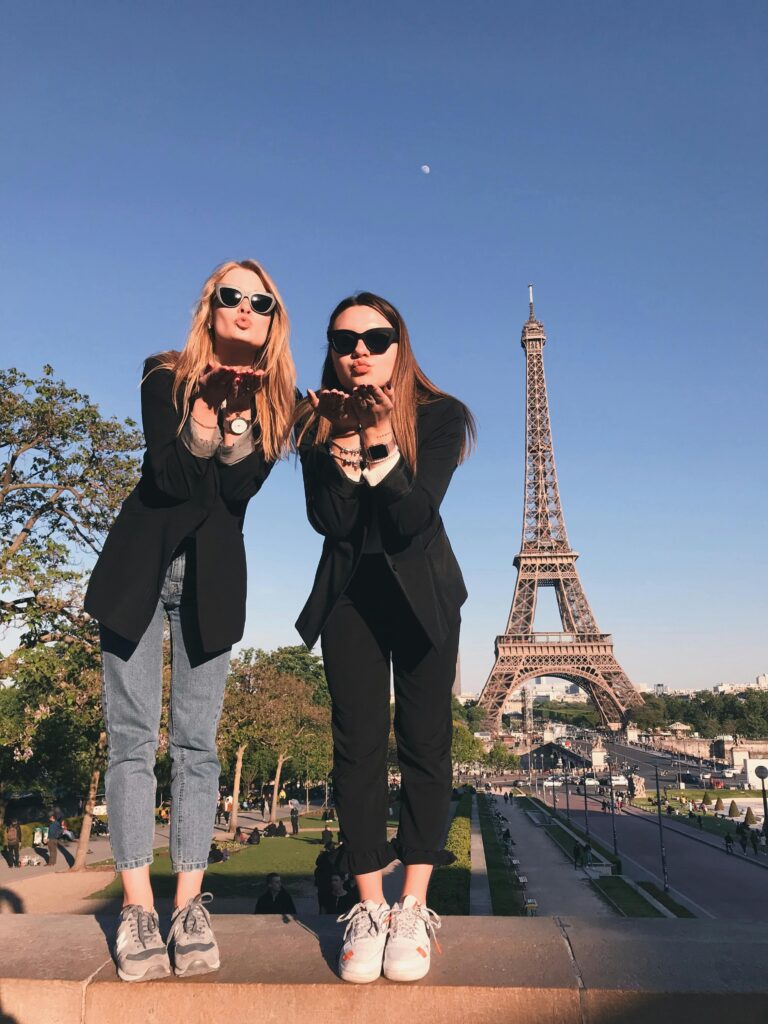 Two young women posing in front of the Eiffel Tower, enjoying travel and lifestyle experiences in France