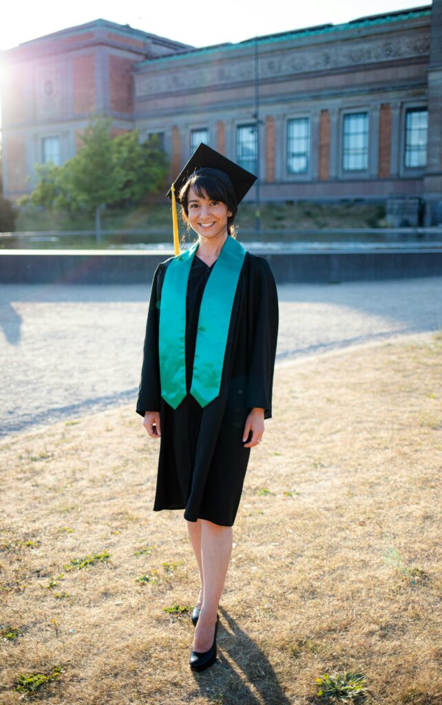Smiling female graduate in black gown with green stole standing outdoors on a sunny day, symbolizing academic success and study abroad opportunities in Denmark.