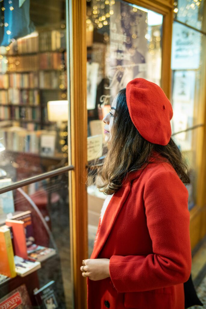 Female student wearing a red beret and coat looking at books in a Paris store, representing lifestyle and daily expenses for students in France.