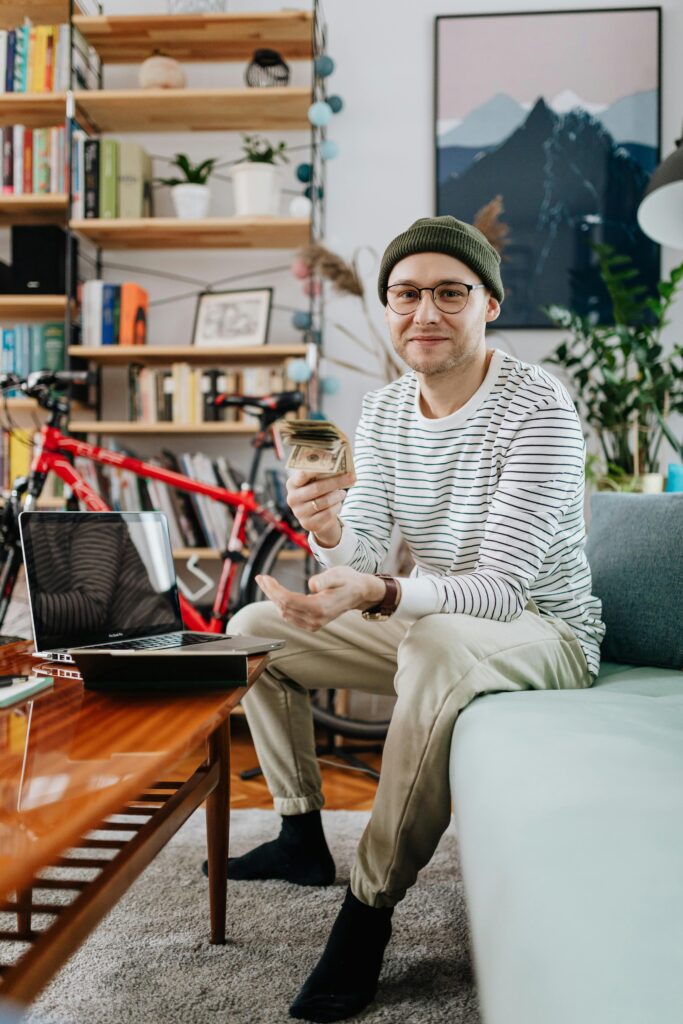 A happy student holding money while sitting near a laptop, representing scholarships and financial aid available for international students studying in Canada.