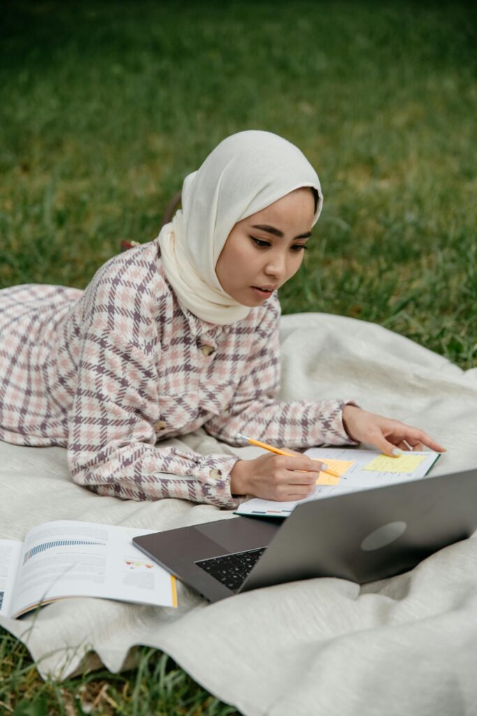 A student in hijab studying outdoors with a laptop and notebook, representing focused study planning for Australia.