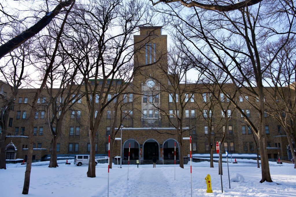 Snow-covered university building surrounded by leafless trees in winter, representing Japan’s serene and disciplined academic environment.