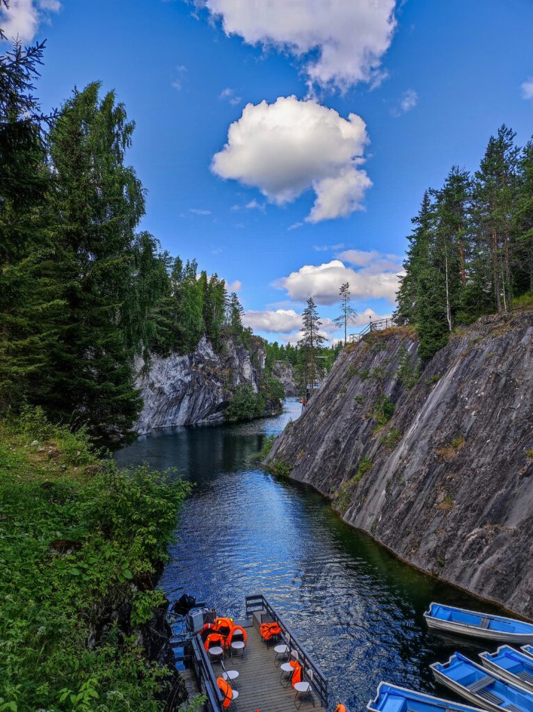 A scenic river flowing between rocky cliffs surrounded by lush green forests and boats docked at a wooden platform in Finland.