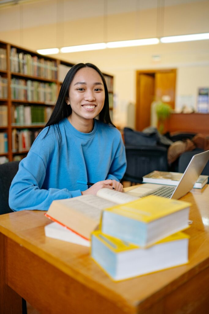 Smiling student studying with laptop and books in library – Study Silently