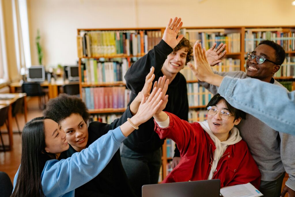 A group of international students smiling and high-fiving in a library, symbolizing teamwork, global learning, and Study Silently’s mission to connect and inspire study abroad students.