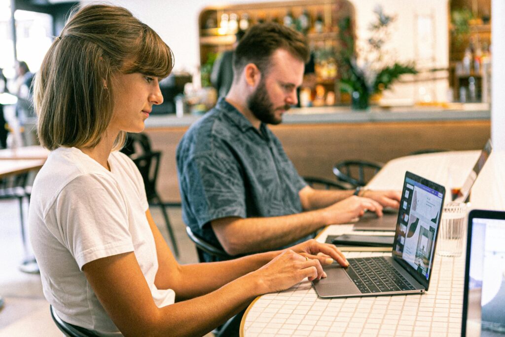 Two students working on laptops in a café while researching universities and planning their study abroad journey.