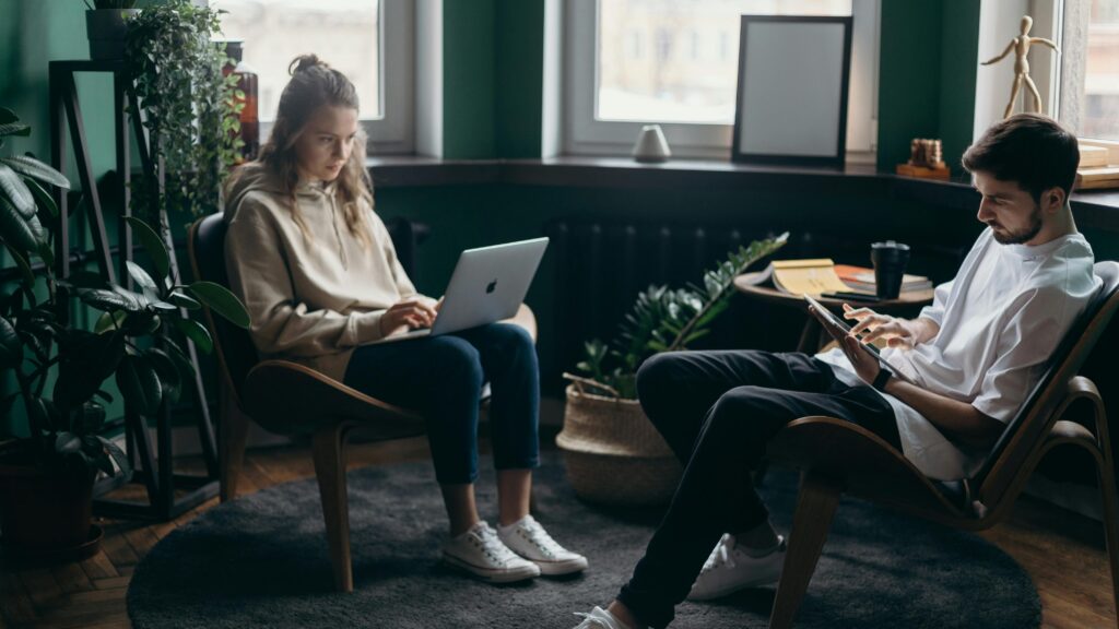 Two students sitting in a cozy room using a laptop and tablet while researching study abroad opportunities and academic updates.