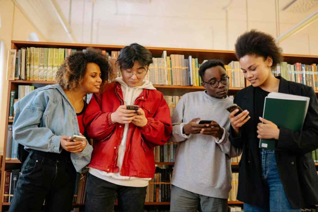 International students checking mobile phones while following Study Abroad News Updates on YouTube in a university library